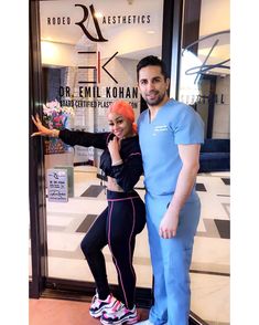 a man and woman posing for a photo in front of a storefront window with their arms around each other