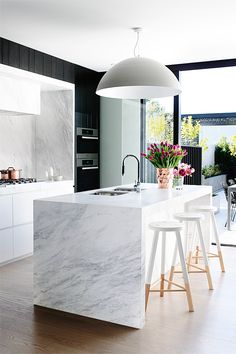 a kitchen with marble counter tops and stools in front of an island that has flowers on it