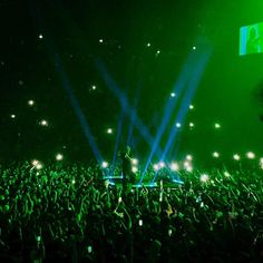 a large crowd at a concert with bright green lights on their shoulders and hands in the air