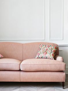 a pink couch sitting in front of a wall with two pillows on top of it