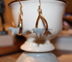 two dolphins dangling from gold hoop earrings on a white cup