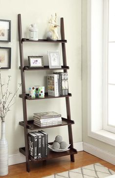 a leaning shelf with books and pictures on it next to a vase filled with flowers