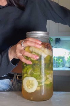 a woman is holding a jar full of pickles and lemons in the kitchen