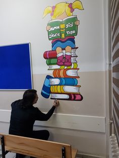 a woman sitting on a bench in front of a wall with books painted on it