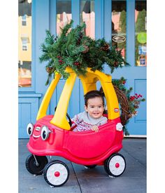 a little boy sitting in a toy car with a christmas tree on top