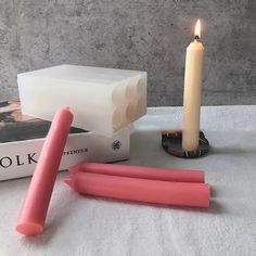 two candles, one pink and one white are sitting on a table next to some books