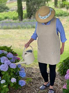 an older woman is watering flowers in the garden with a hat on her head and blue jeans