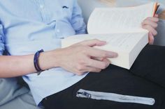 a person sitting down reading a book with a pen in their hand while holding an open book