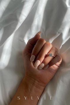 a woman's hand with a diamond ring on her left wrist, resting on a white sheet