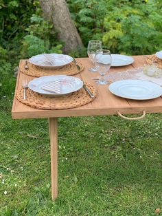 a wooden table with plates and glasses on it in the middle of a grassy area