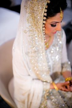 a woman wearing a white veil and holding a gold ring in her hand while sitting on a chair