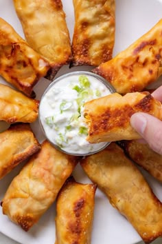 a person dipping sauce on some appetizers in a white plate with other food items