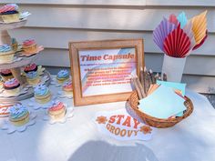 a table topped with cupcakes next to a sign and paper fans on top of it