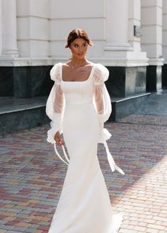 a woman in a white wedding dress standing on a brick walkway with her arms outstretched