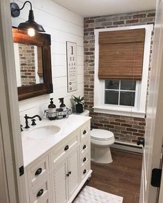 a bathroom with brick walls and white fixtures, including a sink, toilet, and window