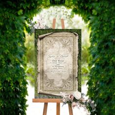 an easel with flowers and greenery in front of a wedding card on it