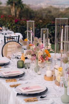 the table is set with candles, plates and vases filled with flowers on it