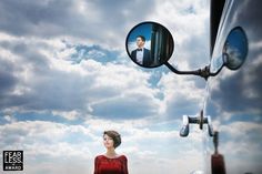 a woman standing in front of a truck with a man's face reflected in the mirror