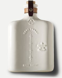 a white ceramic flask with an anchor on the front and brown leather strap around it