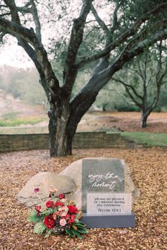 a memorial stone with flowers on it in front of a tree and some fallen leaves