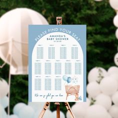 a blue and white baby shower sign sitting on top of a wooden easel in front of balloons