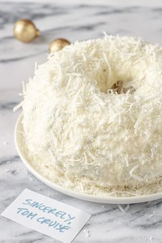 a white cake with coconut on top sitting on a marble table next to gold ornaments