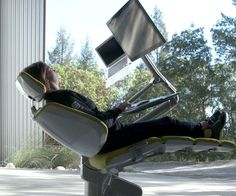 a man laying on top of a white chair in front of a computer desk with a monitor