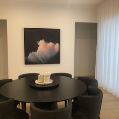 a dining room table with black chairs and a painting on the wall