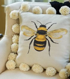 a white pillow with a yellow bee on it and pom - poms around the edges