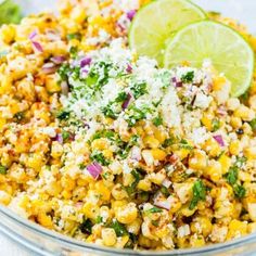 corn salad with lime wedges and parmesan cheese in a glass bowl on a table