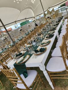 a long table set with green and gold place settings for an outdoor wedding or reception