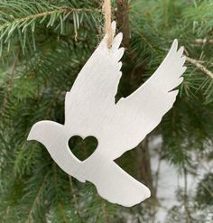 a white bird ornament hanging from a pine tree with a heart cut out of it