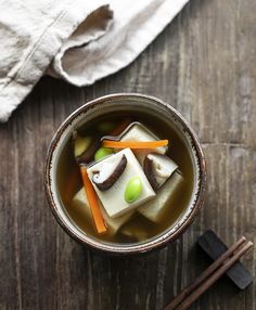 a cup filled with soup next to chopsticks on top of a wooden table