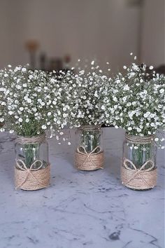 three mason jars with baby's breath flowers tied in twine and burlap