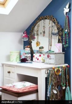 a white desk topped with a mirror and lots of necklaces on top of it