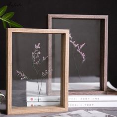 two wooden frames with flowers in them sitting on a table next to books and a plant