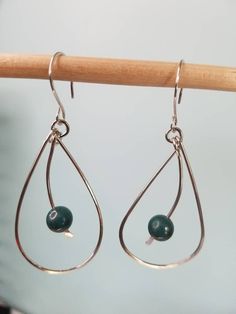 two green beads hanging from silver hoops on a wooden stick with a white wall in the background