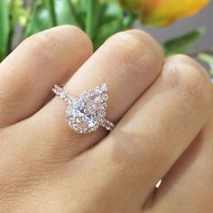 a woman's hand with a diamond ring on top of her finger and flowers in the background