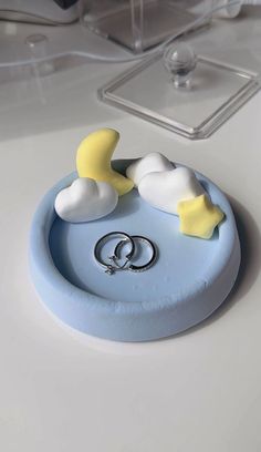 two wedding rings sitting on top of a blue ring holder with white clouds and yellow stars