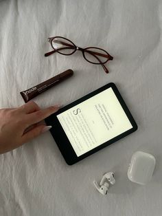 a person is holding an electronic device on a table with eyeglasses and other items