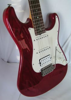 a red electric guitar sitting on top of a white sheet