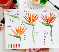 a person is holding up some watercolors on paper with flowers in the background