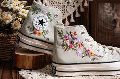 a pair of white sneakers with flowers painted on them sitting next to a basket of daisies