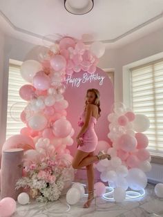 a woman standing in front of balloons with the words happy birthday written on it's wall