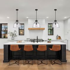 a large kitchen with an island and bar stools next to it, along with three lights hanging from the ceiling