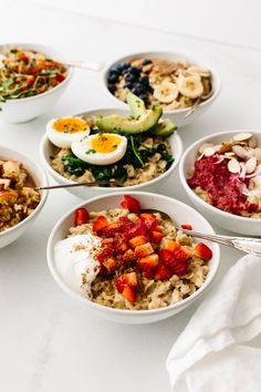 six bowls filled with different foods on top of a white countertop next to utensils