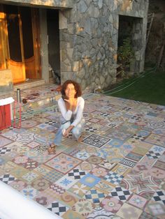 a woman sitting on top of a tiled floor next to a fire place in front of a building