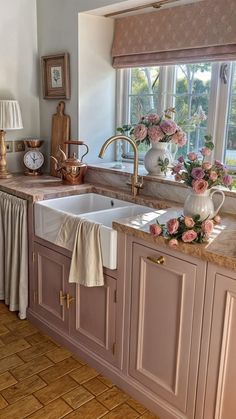 a kitchen with pink cabinets and flowers on the counter top, along with a window