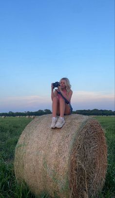 a woman sitting on top of a hay bale with a camera in her hand