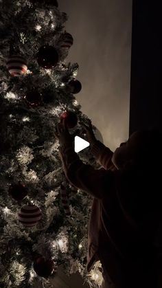 a man standing in front of a christmas tree with lights on it and ornaments hanging from the branches